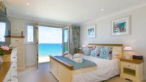 Une chambre avec un grand lit, une table de chevet, une commode et une vue sur la mer.