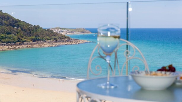 Une table avec un verre à vin et un saladier de fruits sur un balcon donnant sur une plage et la mer.