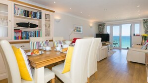 Un salon moderne avec une table à manger en bois, des canapés blancs et une bibliothèque remplie de livres.