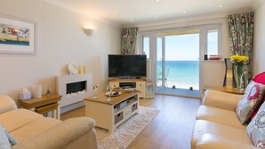 Un salon équipé d’un téléviseur, d’un canapé et offrant une vue sur la mer grâce à une porte vitrée.