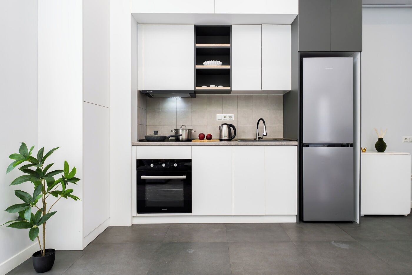 A modern kitchen with white cabinets, a stainless steel refrigerator, an oven, and a sink.