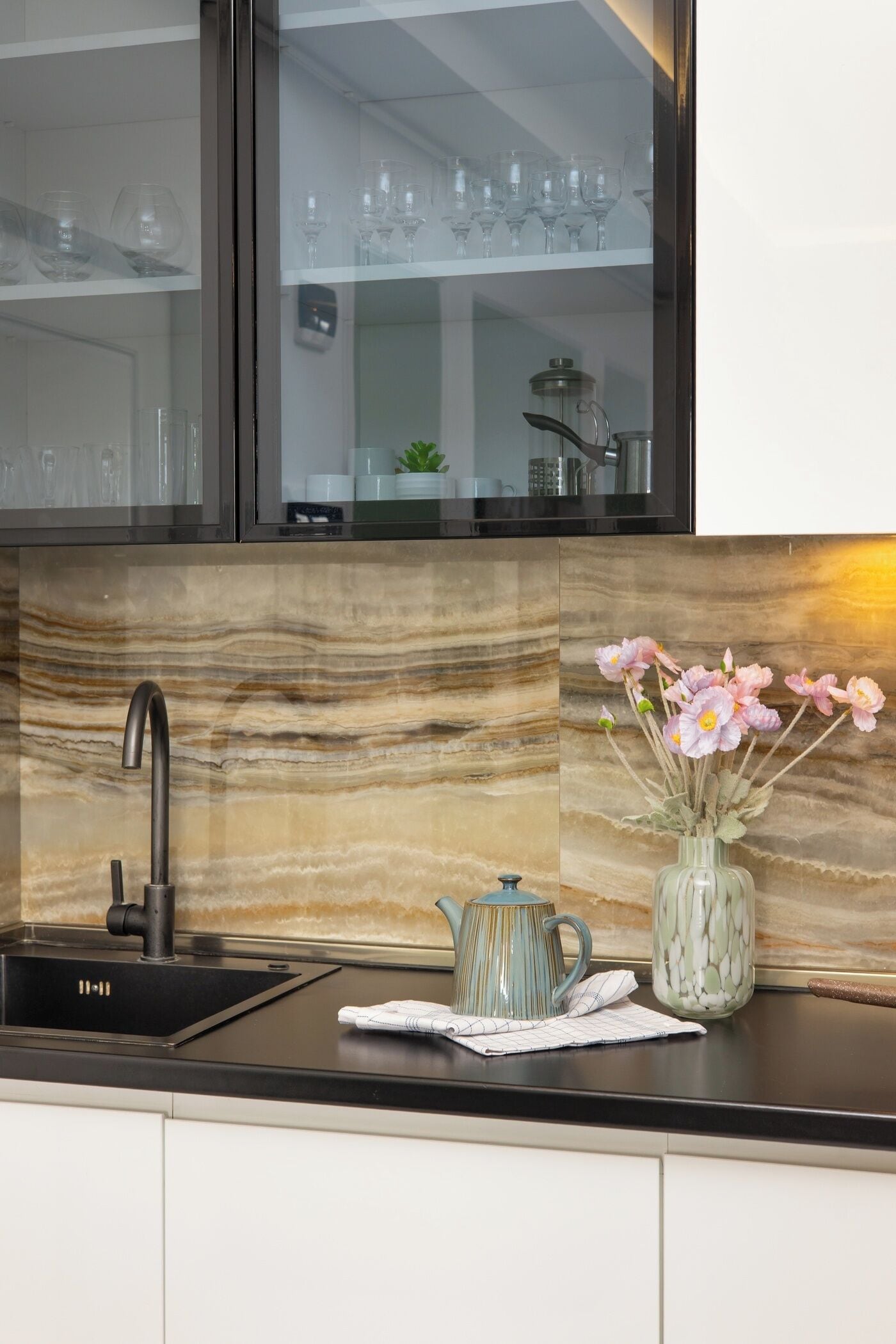 A kitchen with a modern black sink, a marble backsplash, and a vase with flowers on the counter.