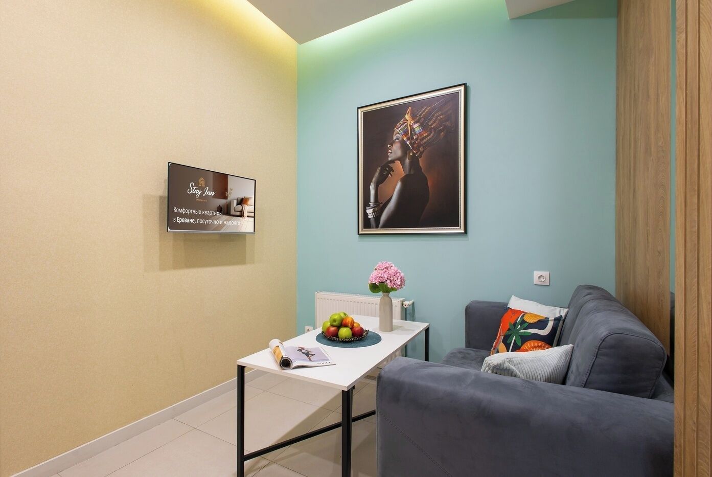 Una sala de estar moderna con un sofá gris, una mesita con un jarrón de flores, una obra de arte enmarcada en la pared y un cartel con texto.