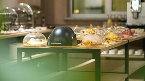 A buffet setup with various food items under glass domes, a modern kitchen in the background, and a green-toned ambiance. - Central Park Resident (Bishkek)