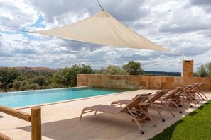 A pool area with lounge chairs and a large shade sail, surrounded by a stone wall and a view of the countryside. - Deluxe Double Room with Balcony (Veiros)
