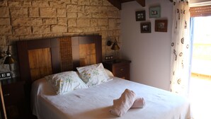 A bedroom with a stone wall, a wooden headboard, a bed with white bedding, a bedside table, and a lamp. - Casa Rural Julia Y Chloé (MOLVÍZAR)