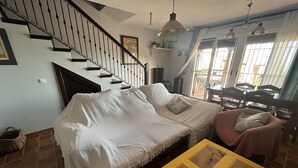 A living room with a covered sofa, a yellow table, and a staircase with black railings. - Casa Rural Julia Y Chloé (MOLVÍZAR)