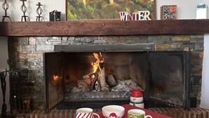 A fireplace with a stone surround, a table with a glass top, and a framed picture above the fireplace. - Casa Rural Julia Y Chloé (MOLVÍZAR)