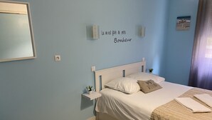 A bedroom with a bed, bedside tables, a nightstand, a chair, and a wall-mounted light fixture. - La dame de coeur (Soulac-sur-Mer)