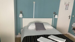A bed with a white headboard, a grey blanket, and two white towels on a striped bedspread. - La dame de coeur (Soulac-sur-Mer)