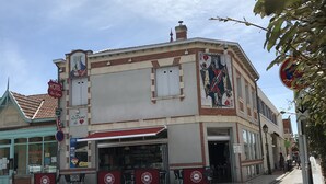 A hotel with a red awning, a mural on the side, and a sign indicating a no parking zone. - La dame de coeur (Soulac-sur-Mer)