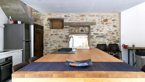 A modern kitchen with a stone wall, a wooden dining table, and a refrigerator. - Architect's house - 10000m2 garden and undergrowth (Bains-sur-Oust)