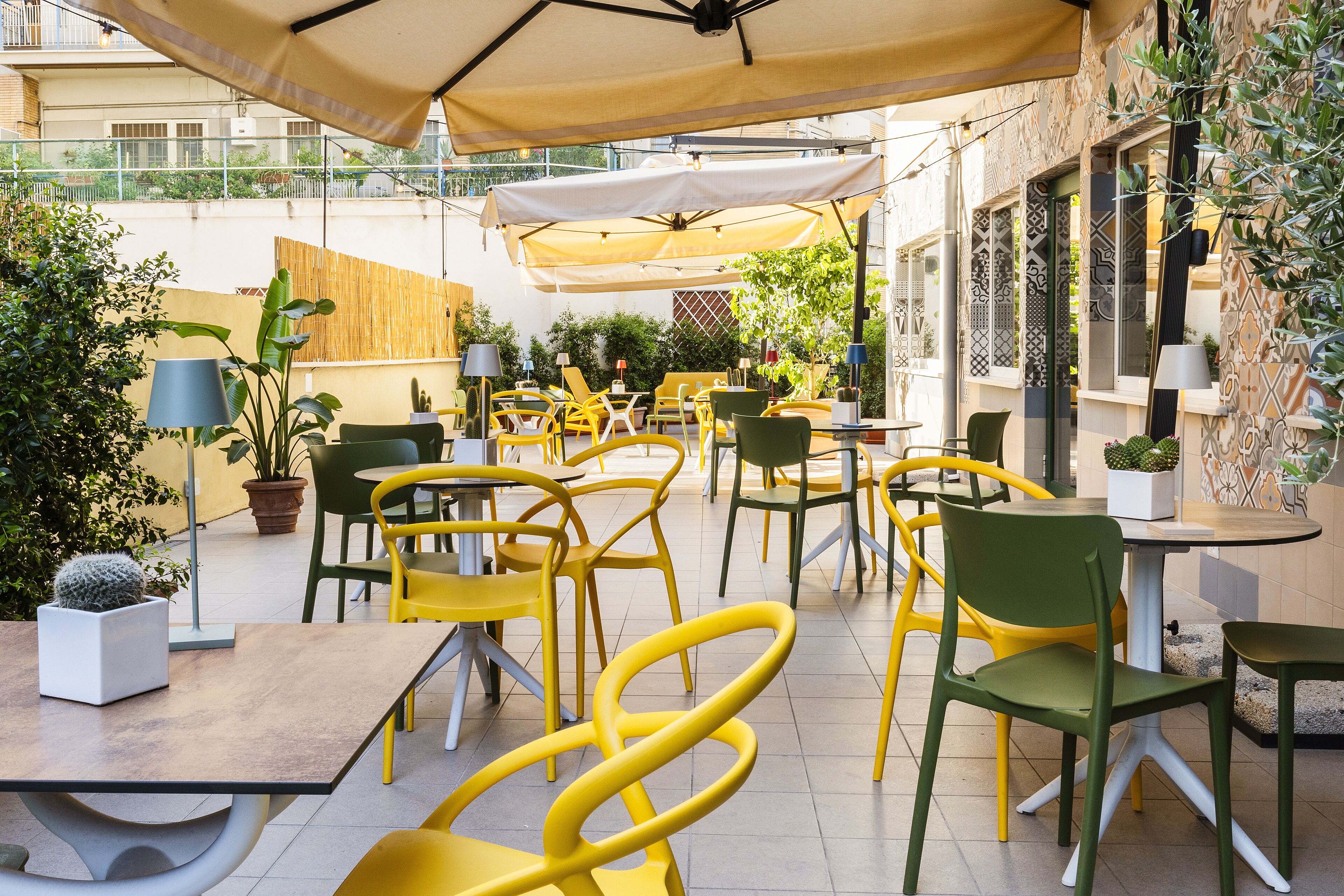 Un caffè all'aperto con sedie, tavoli e ombrelloni gialli e verdi.