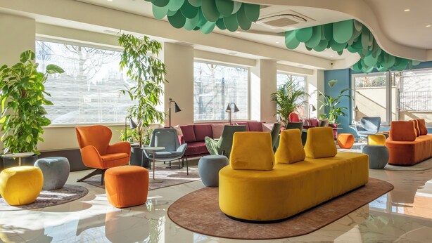 A modern lobby with a yellow sofa, orange chairs, and green ceiling decorations. - Adesso Hotel (Rome)