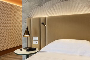 Una camera d'albergo con un letto, un comodino con una lampada, un telecomando e una parete con motivo geometrico.