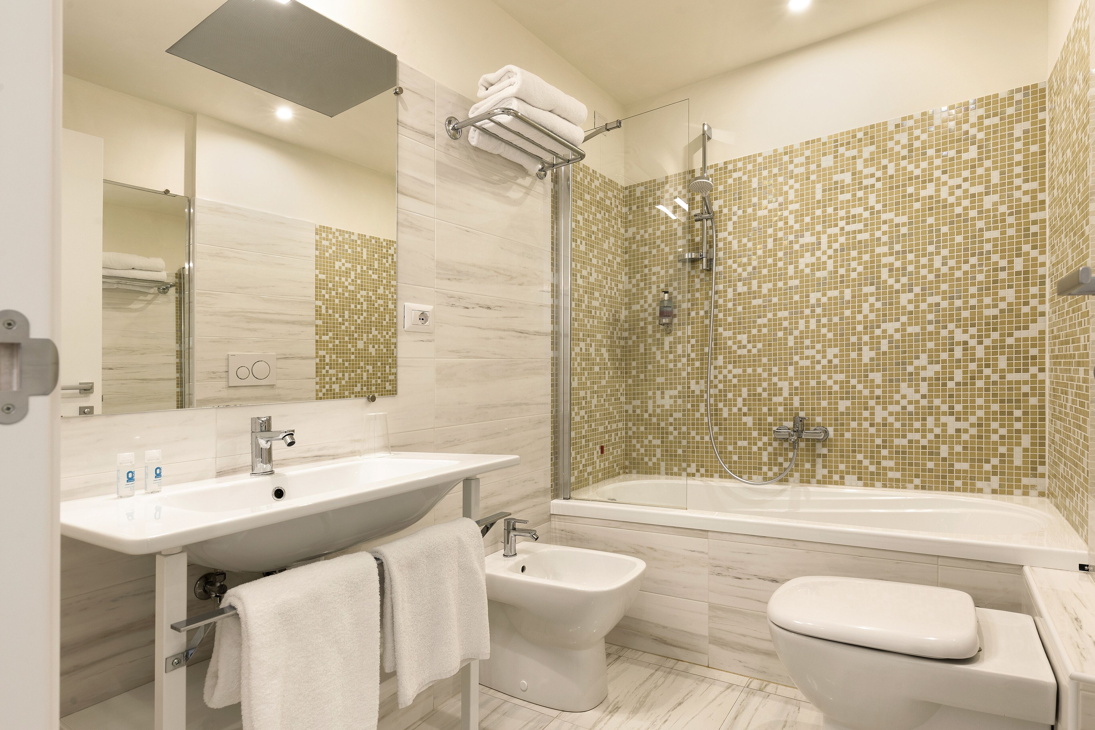 Un baño moderno con lavamanos, bidé, inodoro y zona de ducha con mosaicos.