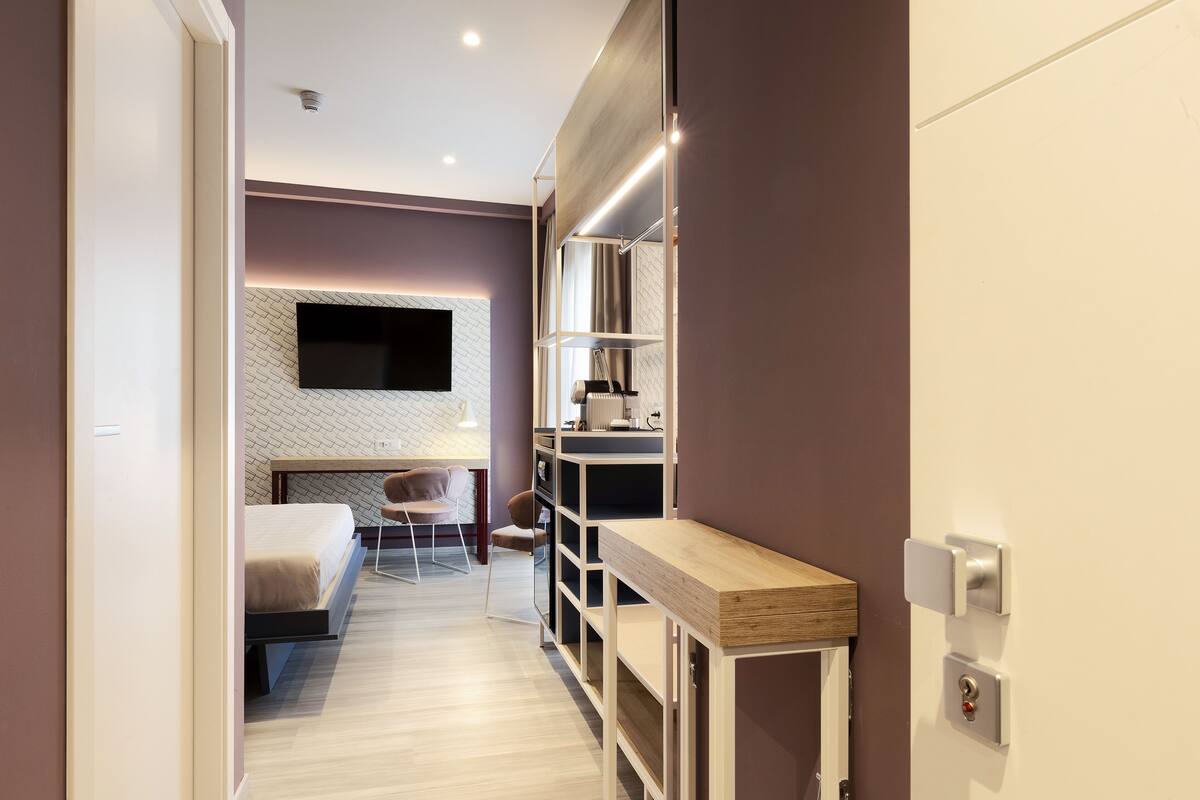 Una habitación de hotel moderna con una cama, un escritorio, una silla y un televisor montado en la pared.