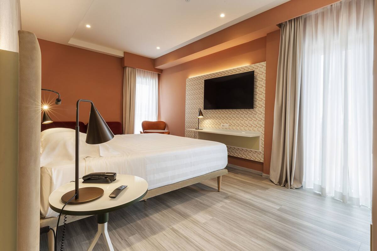 Una habitación de hotel moderna con cama, mesita de noche, lámpara y televisor montado.