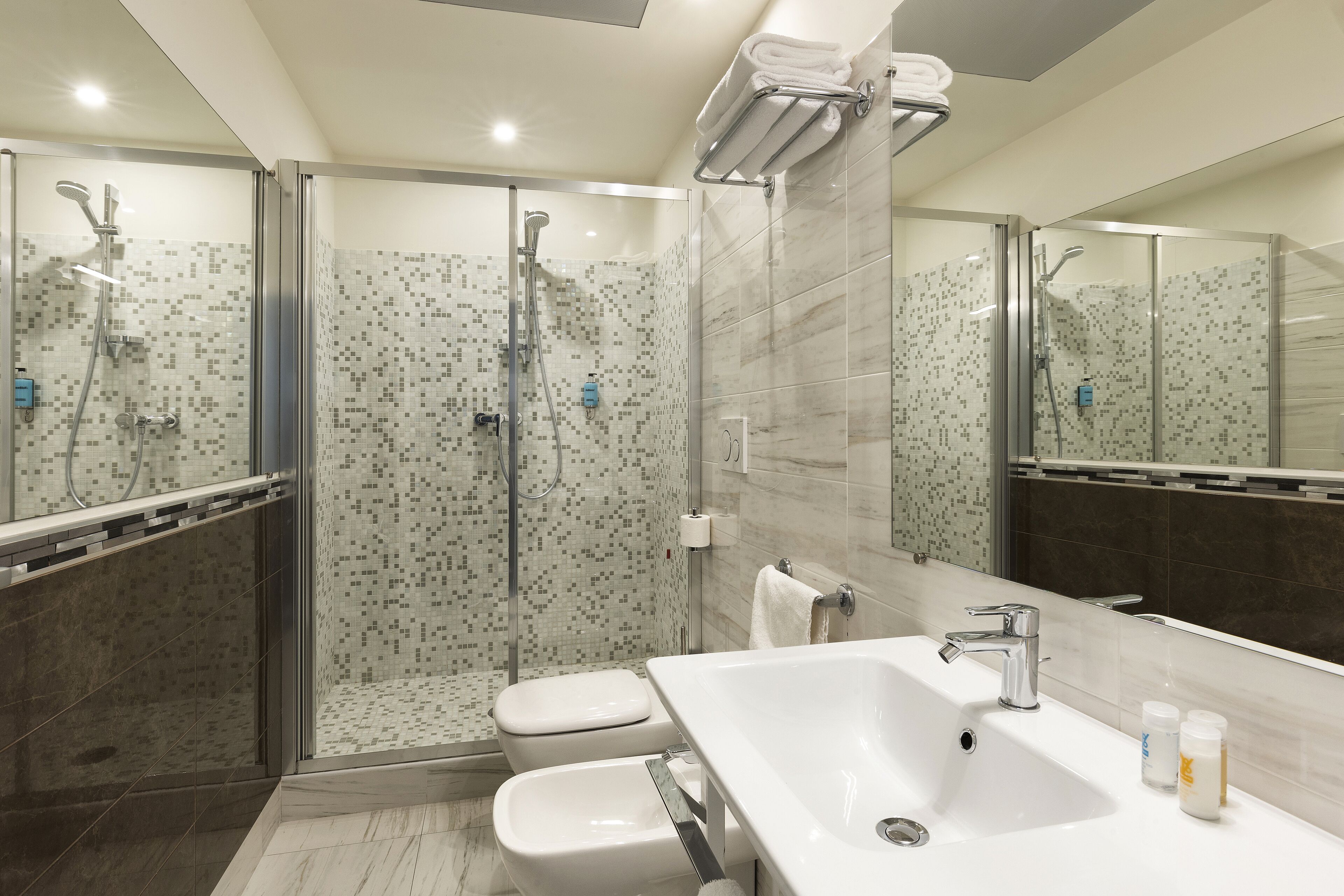 Un bagno moderno con cabina doccia in vetro, lavabo bianco e uno specchio grande.
