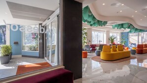 A modern lobby with a glass entrance, a red bench, and a yellow sofa. - Adesso Hotel (Rome)
