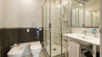 Un baño moderno con ducha de mampara de vidrio, lavamanos blanco y un bidé.