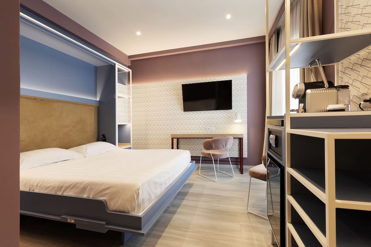 Un dormitorio moderno con una cama, un escritorio, una silla y un televisor instalado en la pared.