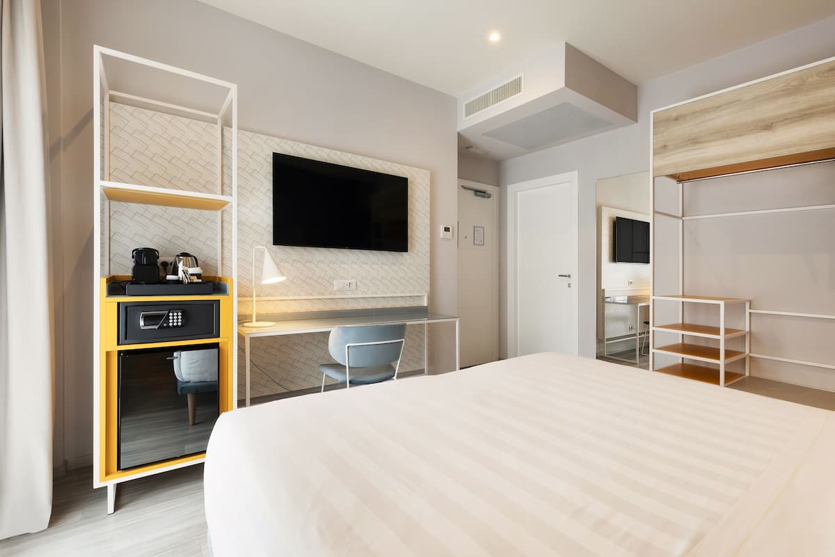 Una habitación de hotel moderna con una cama grande, un escritorio con un televisor de pantalla plana, un microondas y un rincón de descanso con una silla.