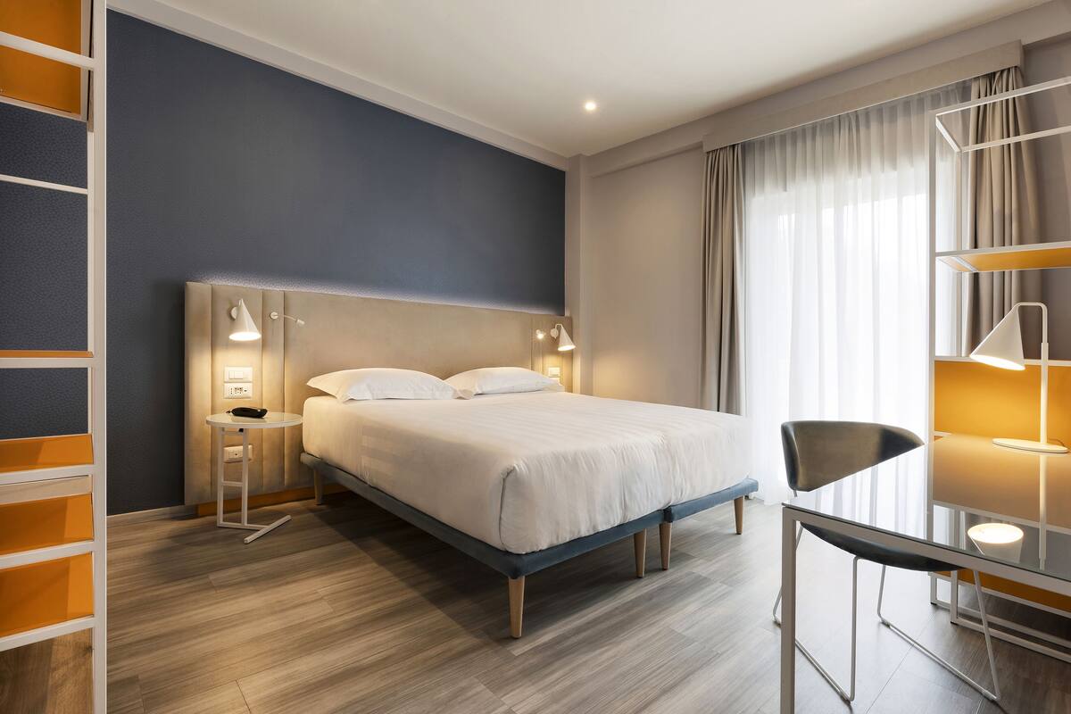 Una habitación de hotel moderna con una cama grande, mesitas de noche, un escritorio y una silla.