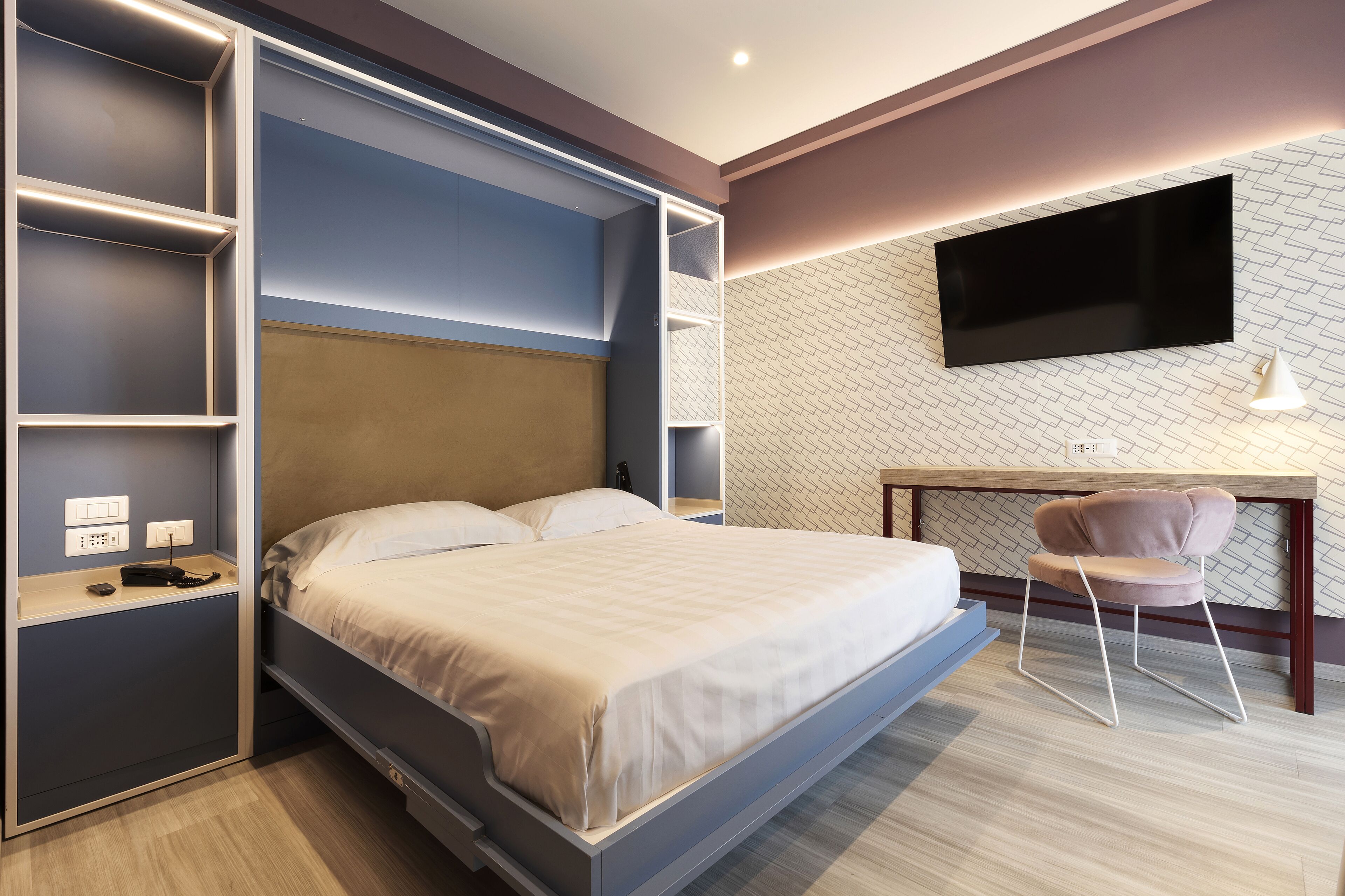 Habitación de hotel moderna con cama, estantes empotrados, escritorio y televisor.