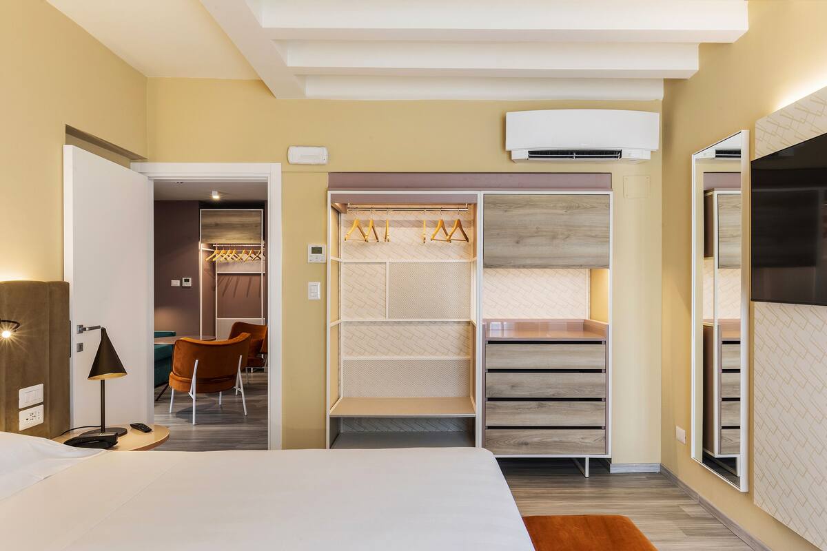 Habitación de hotel con cama, escritorio, silla, armario con espacio para colgar y espejo.