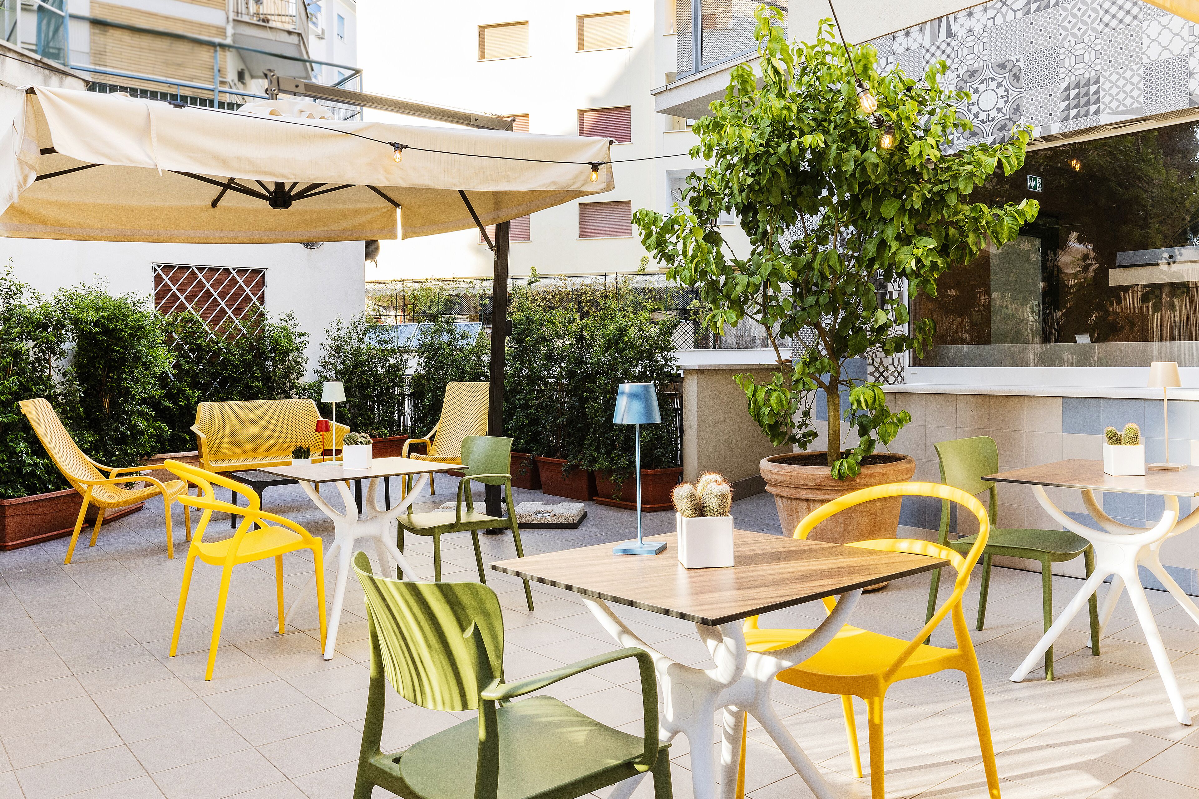 An outdoor patio with yellow and green chairs, a table, and a large umbrella.