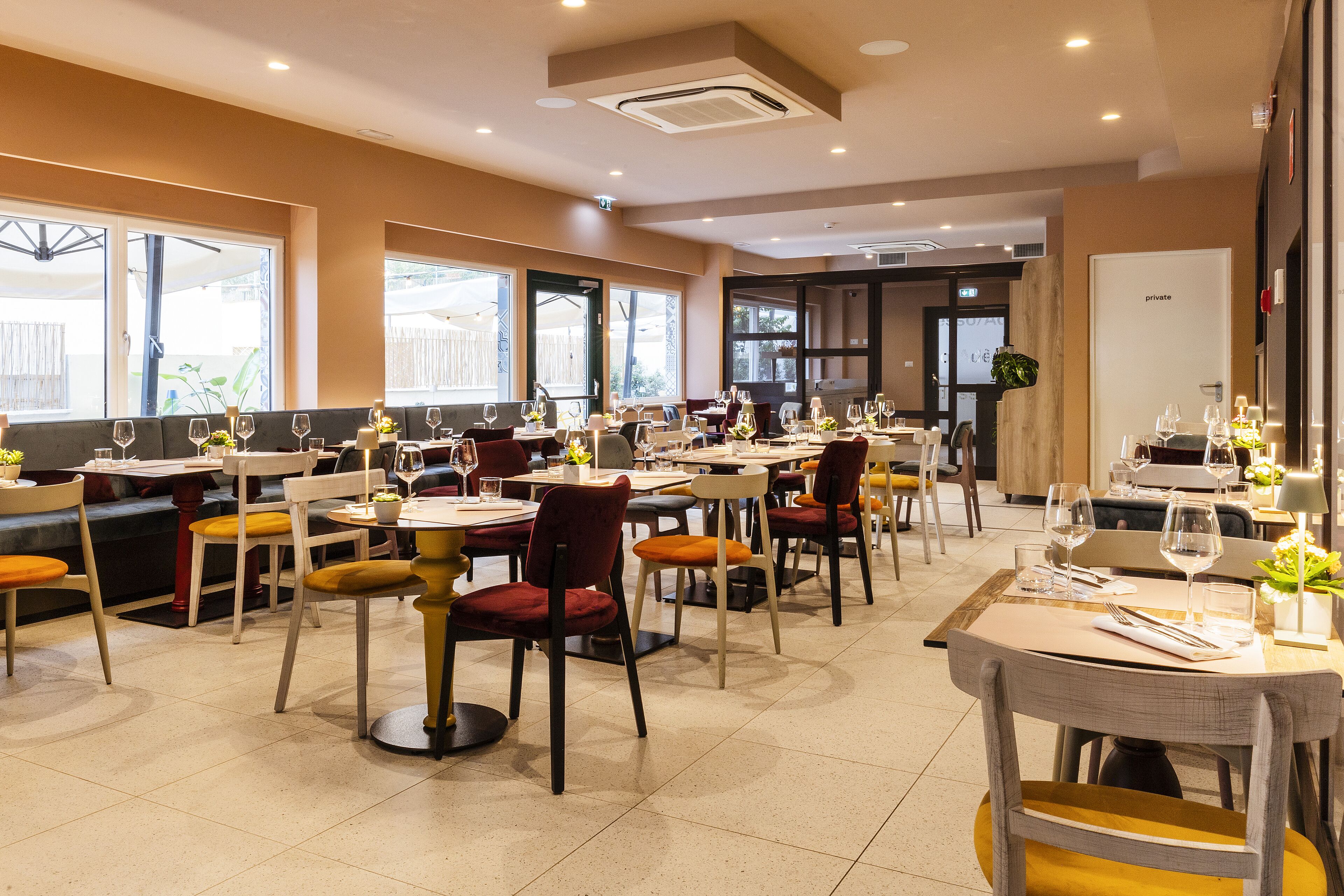 Un restaurante con varias mesas y sillas, ventanas amplias y una sala privada.