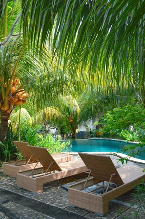 A poolside area with wicker lounge chairs and a pool. - Tarzan Marriott On Penida (Penida Island)