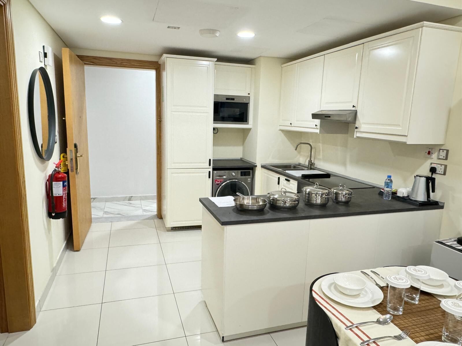 Una cocina moderna con armarios blancos, una isla central con ollas, un microondas y un fregadero.