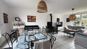 A modern living room with a glass dining table, a sofa, a TV, and a fireplace. - La Mandragora - Atelier d’art et poésie (Vernon)
