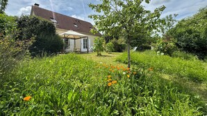 A house with a covered patio, surrounded by lush greenery and wildflowers. - La Mandragora - Atelier d’art et poésie (Vernon)