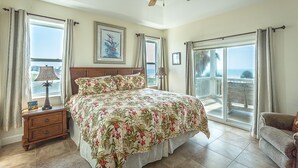 A bedroom with a bed, a nightstand, a ceiling fan, and a view of the ocean through large windows. - Paradise Falls here! 4 BR, Elevator, Pool, across the street from beach (ST GEORGE ISLAND)