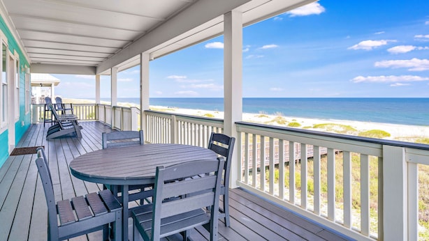 Een overdekt terras met tafel en stoelen, met uitzicht op een strand.