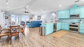 Een moderne keuken met blauwgroene kastjes, een centraal eiland en roestvrijstalen apparatuur.