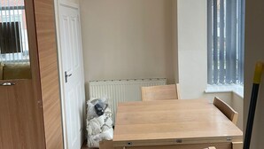 Ein Essbereich mit Holztisch und Stühlen, einem Heizkörper, einem Fenster mit Jalousien sowie einer Treppe.