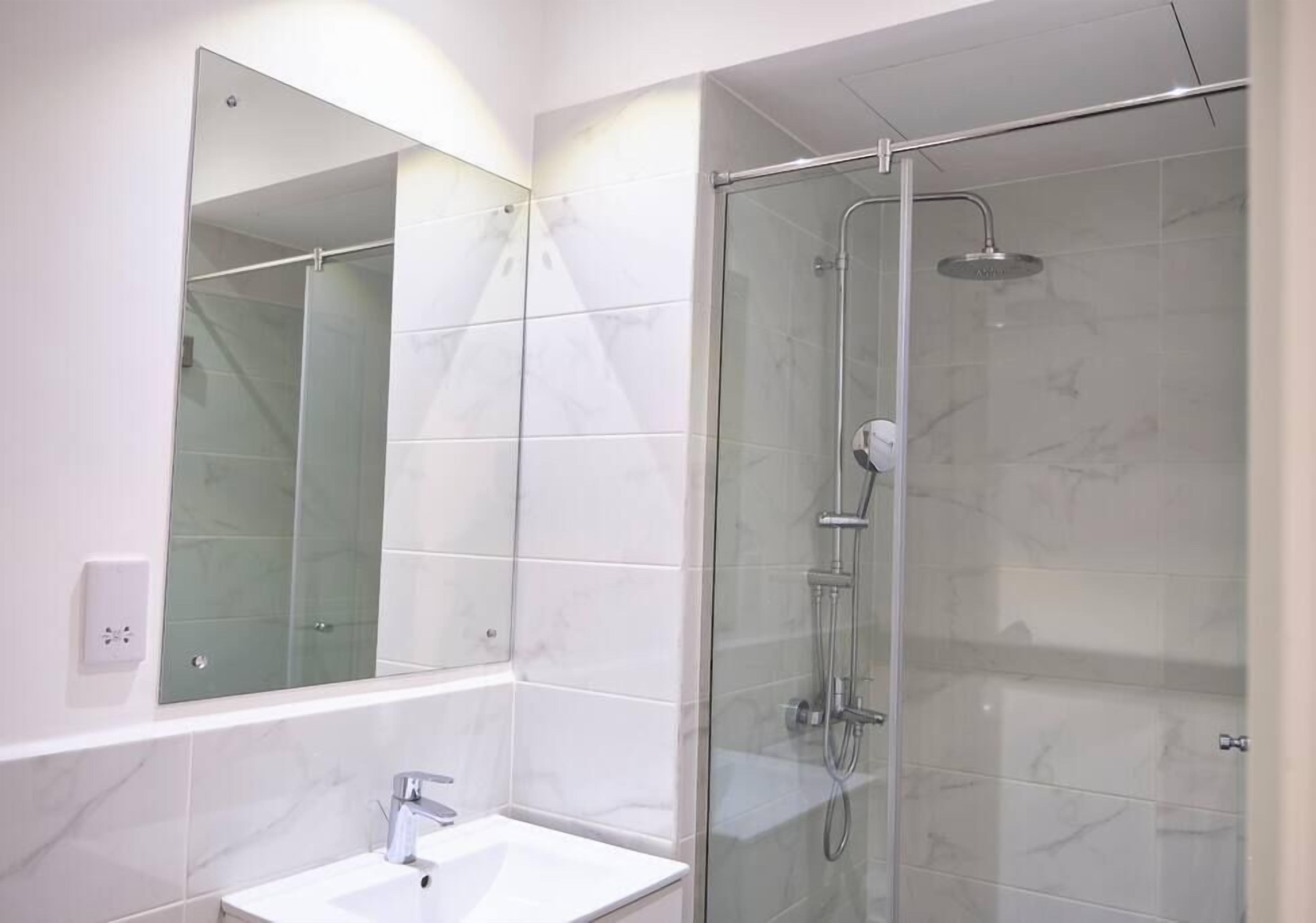 A modern bathroom with a glass-enclosed shower, a white sink, and a large mirror.