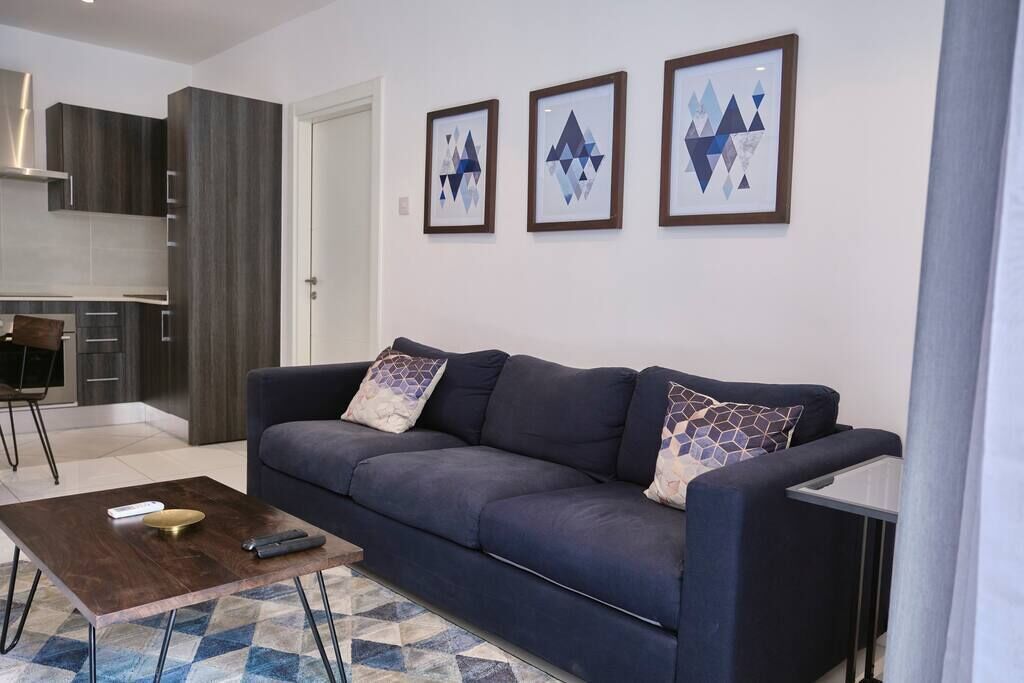 Una sala moderna con un sofá azul oscuro, una mesa de centro y una cocina al fondo.