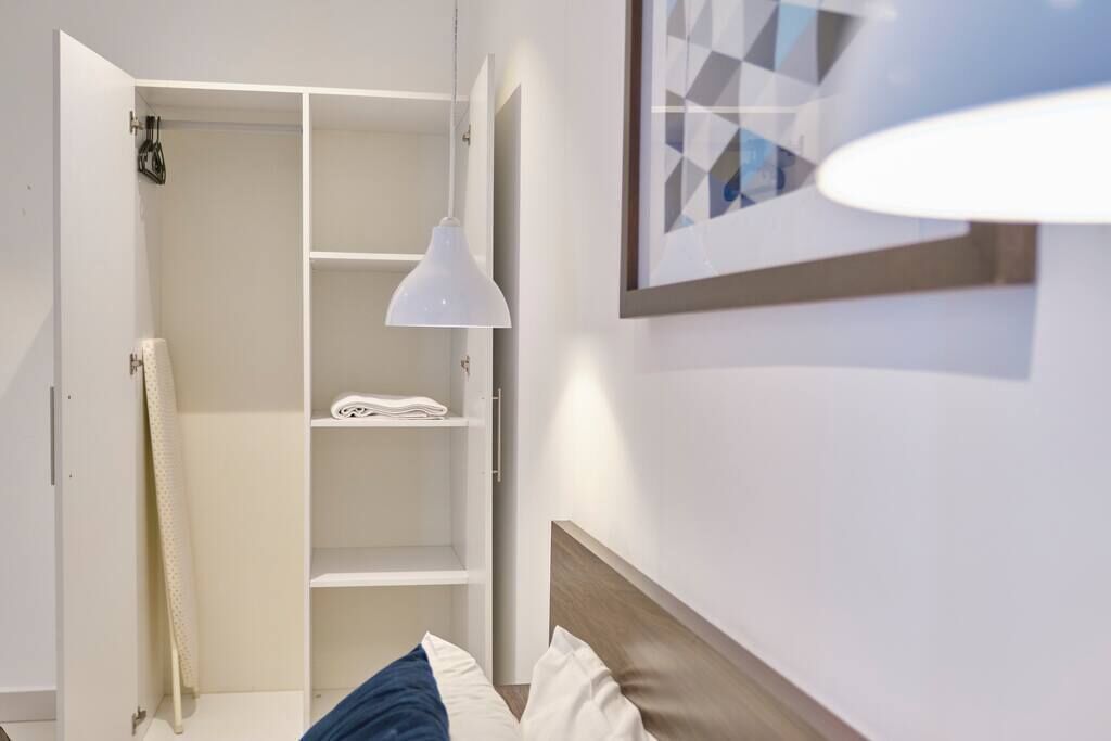 A hotel room with a bed, a wardrobe, and a hanging light fixture.