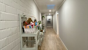 A narrow hallway with white brick walls and wooden flooring. There is a white shelf with toys and a basket on it.