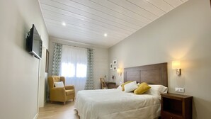 A bedroom with a bed, a chair, a nightstand, a TV mounted on the wall, and a window with curtains.