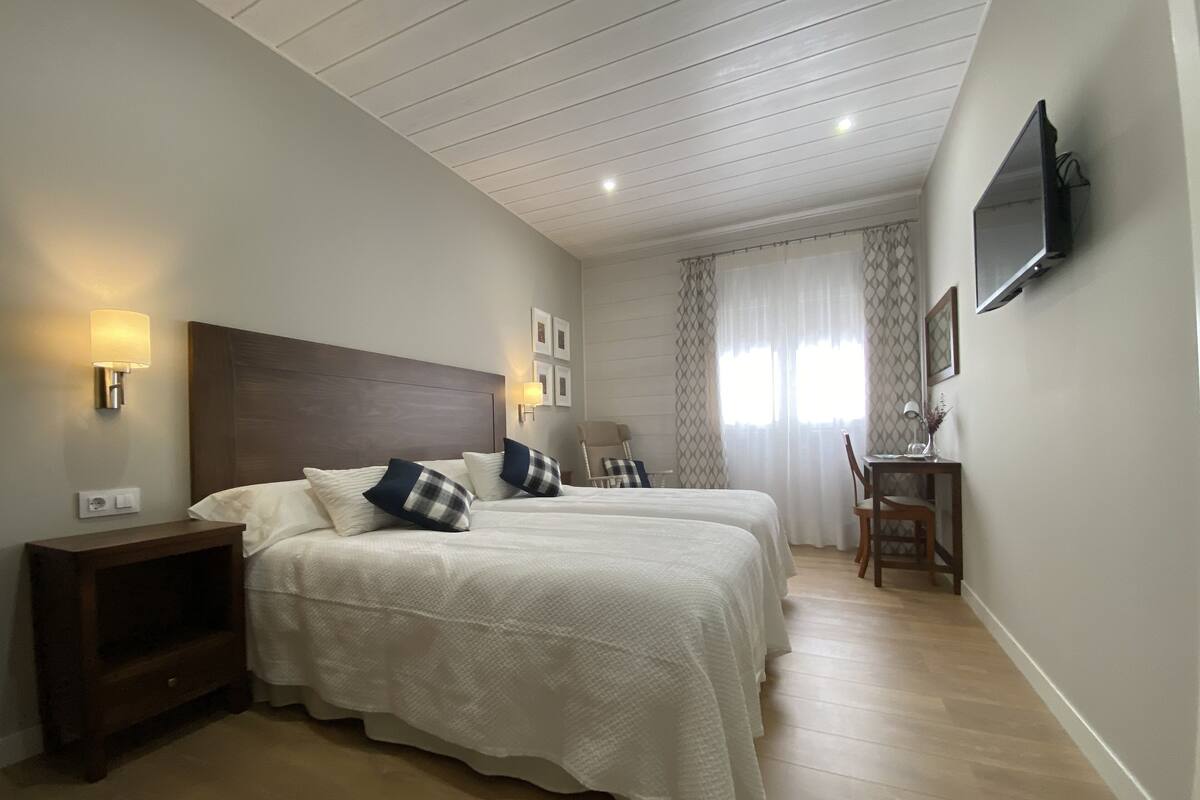 Habitación de hotel con una cama grande, lámparas de noche, un escritorio con una silla y un televisor montado en la pared.