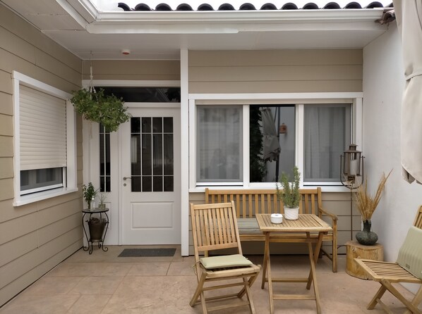 A covered patio with a wooden table and chairs, a bench, and potted plants.