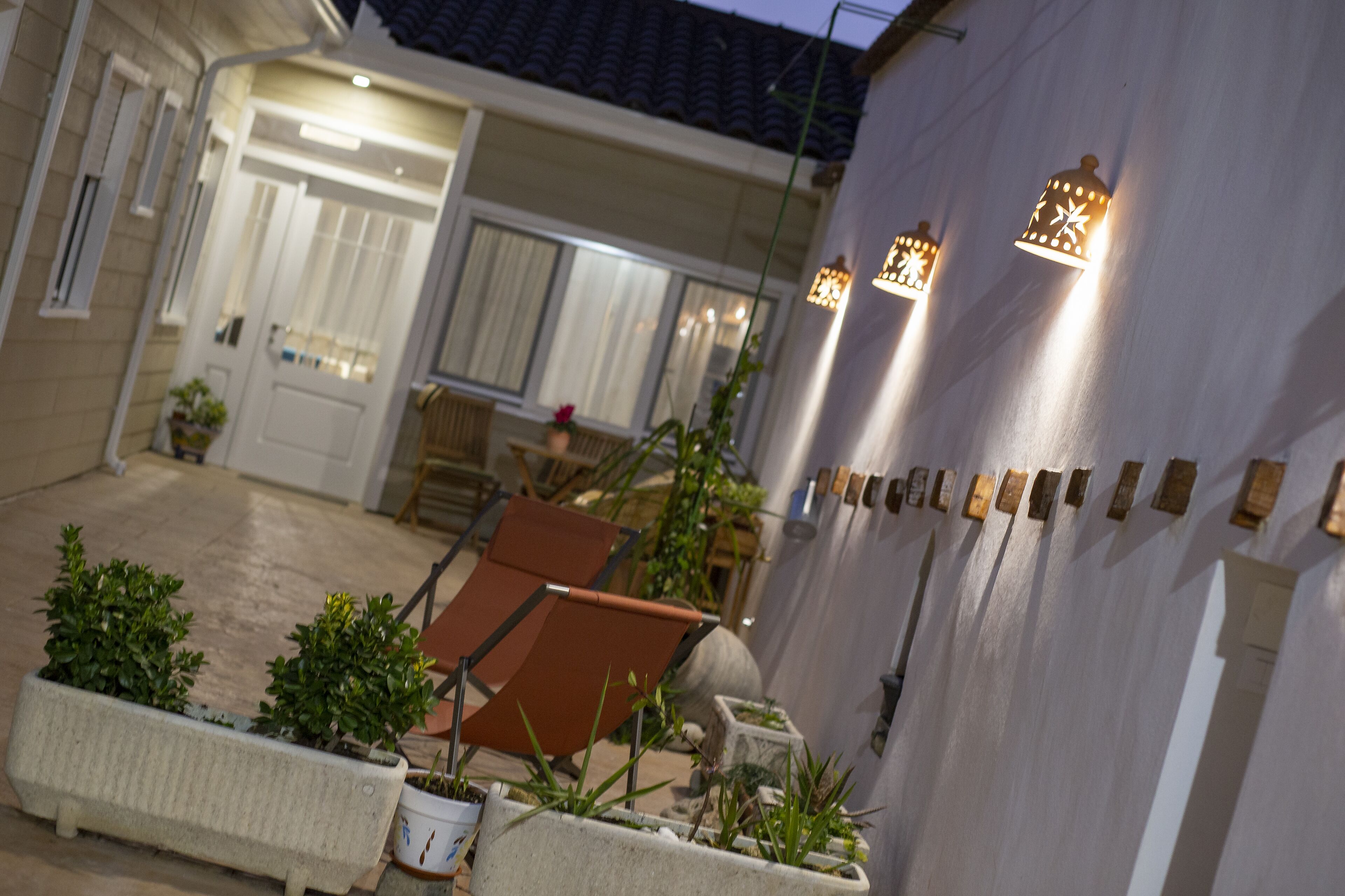 Un patio con plantas en macetas, una silla marrón y luces fijadas a la pared.