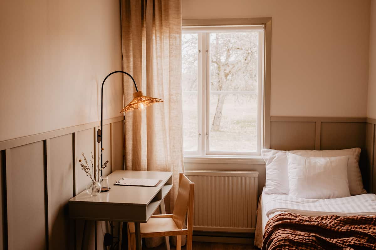 A room with a bed, a desk, a chair, a lamp, and a window with curtains.
