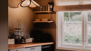 Une cuisine avec des étagères en bois, une machine à café et une fenêtre donnant sur un paysage verdoyant.